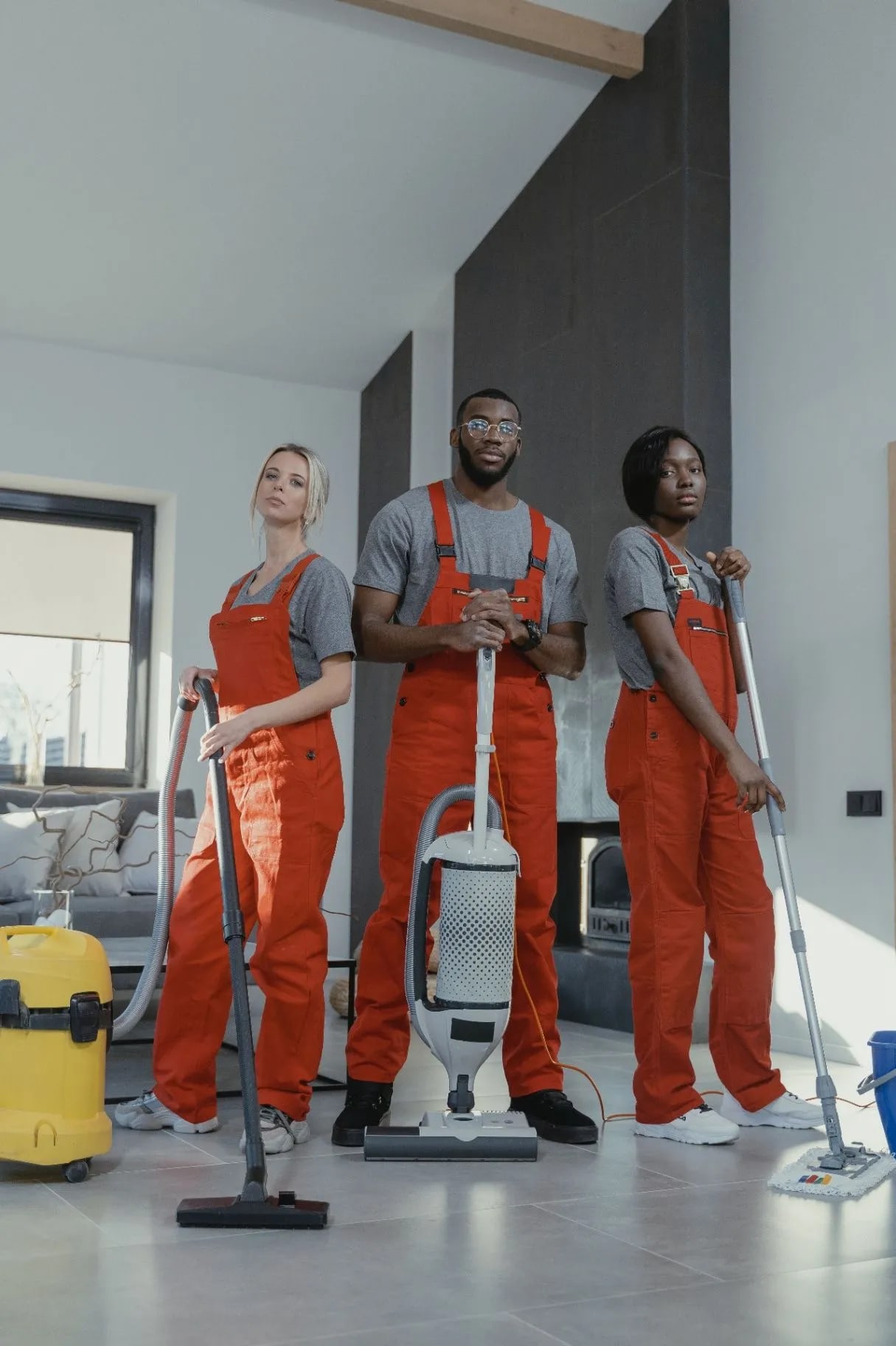Three uniformed cleaners standing together with a vacuum and mops in a bright home